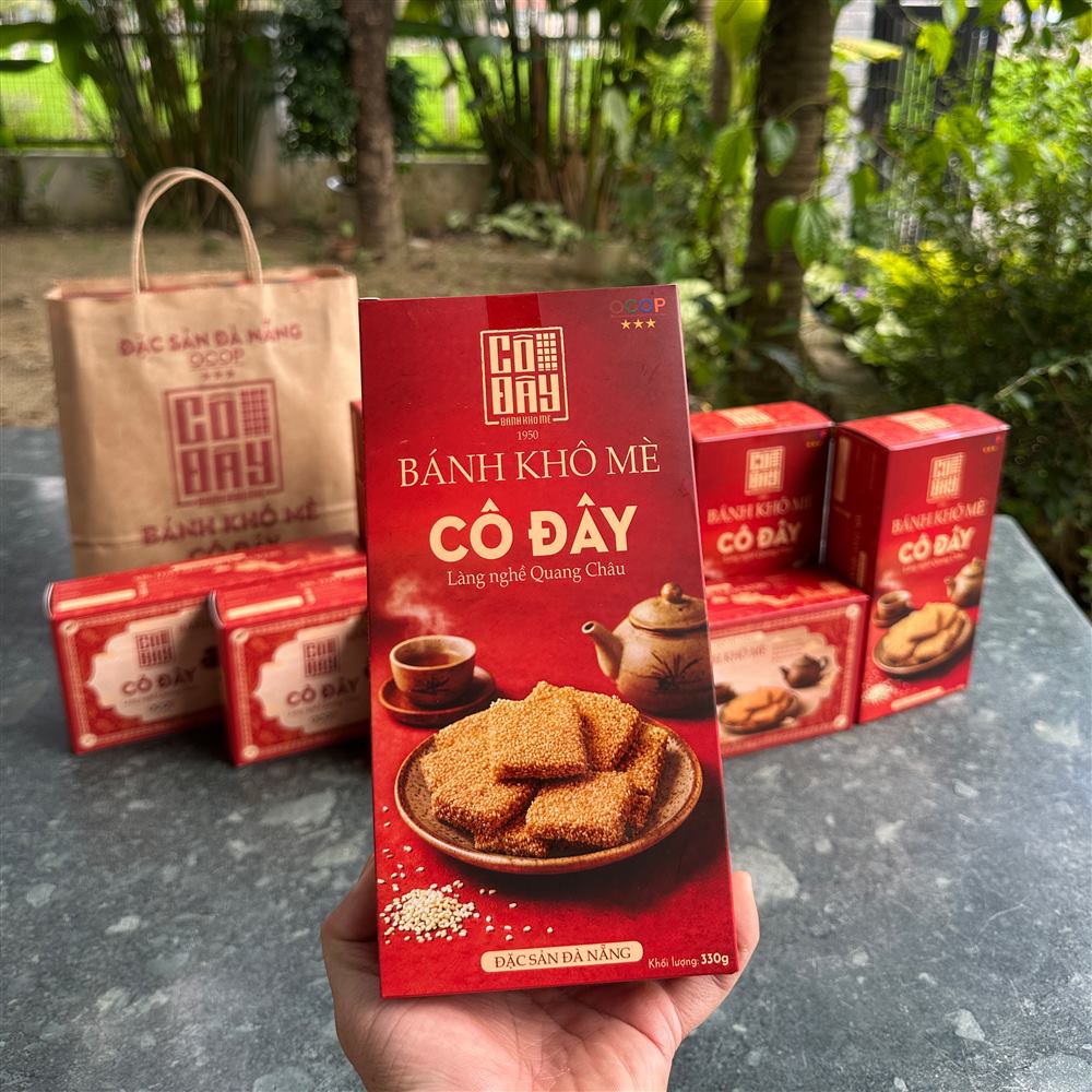 Cầm hộp bánh khô mè Cô Đây ngoài sân vườn